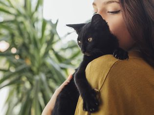 woman holds black cat on her shoulder